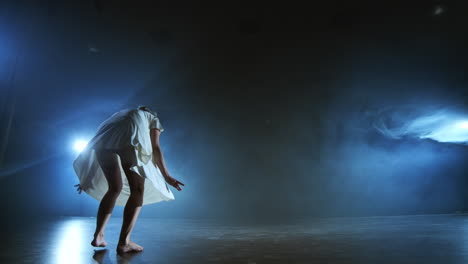 Modern-ballet-dancing-woman-barefoot-doing-spins-and-pirouettes-and-dance-steps-standing-on-stage-in-smoke-in-slow-motion.-Performance-on-stage.