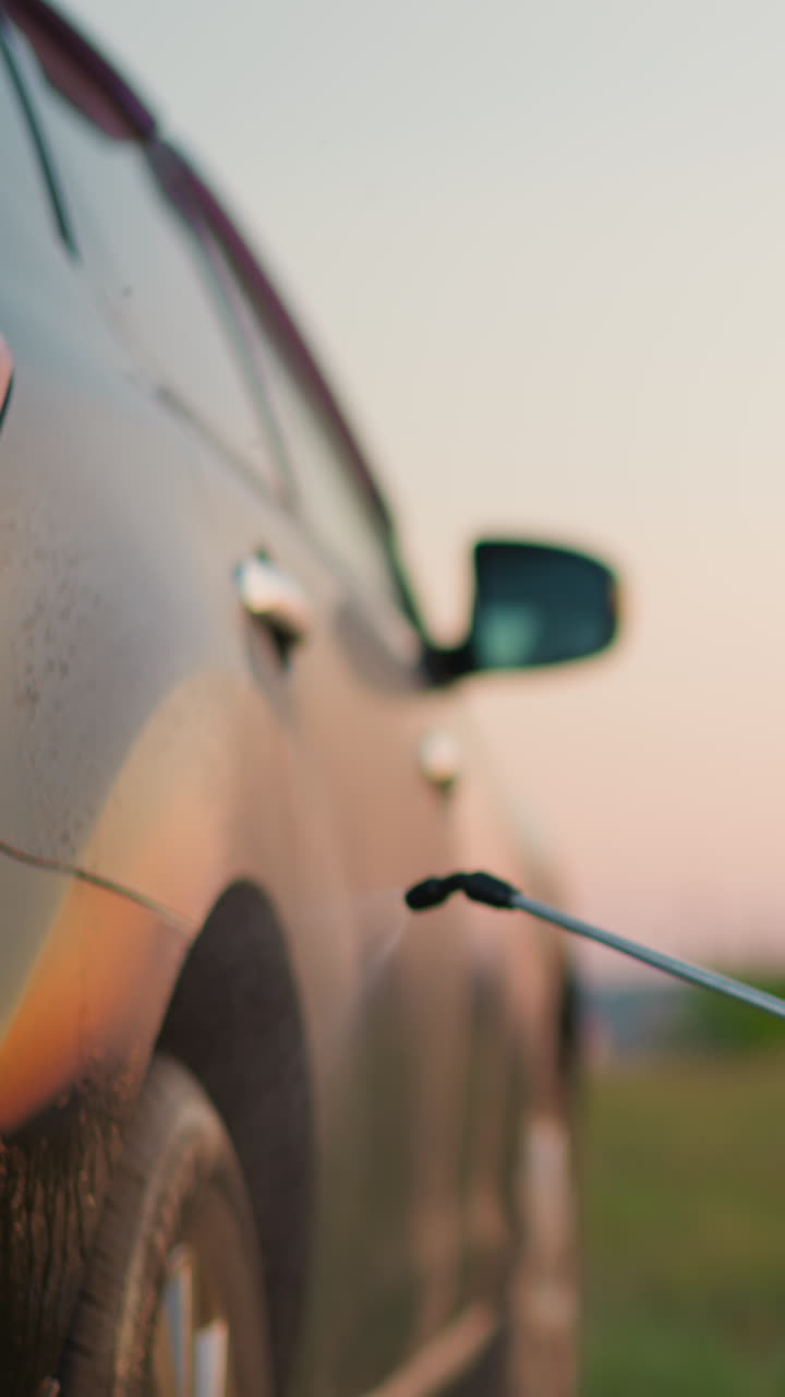 작은 아이는 에서 부모의 차에 물을 뿌립니다. 파란 스웨터를 입은 귀여운 작은 소년은 시골 마당에서 샤워를 가진 자동차를 청소합니다. 아이는 집안 일에 기꺼이 도와줍니다.