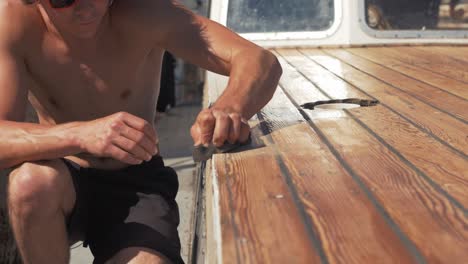 sanding roof planks of timber boat young man blow dust off slow motion