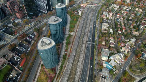 Drohne-Fliegt-Langsam-über-Dem-Titanium-Park-Mit-Den-Drei-Türmen-Von-Santiago-De-Chile,-Herbstverkehr-Bei-Tageslicht,-Stadtbild,-Landmark