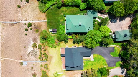 drone footage captures a row of charming cottage-style suburban homes, each with spacious back porches, inviting patio seating areas, lush green yards, and mature trees offering shade and privacy