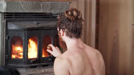 caucasian man half naked placing a piece of cut log in an antique wood fireplace during winter in trondheim, norway