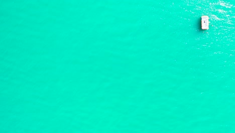 Turquoise-sea-water-texture-with-boat-floating-on-calm-clear-water-near-shore-of-tropical-island-in-Caribbean