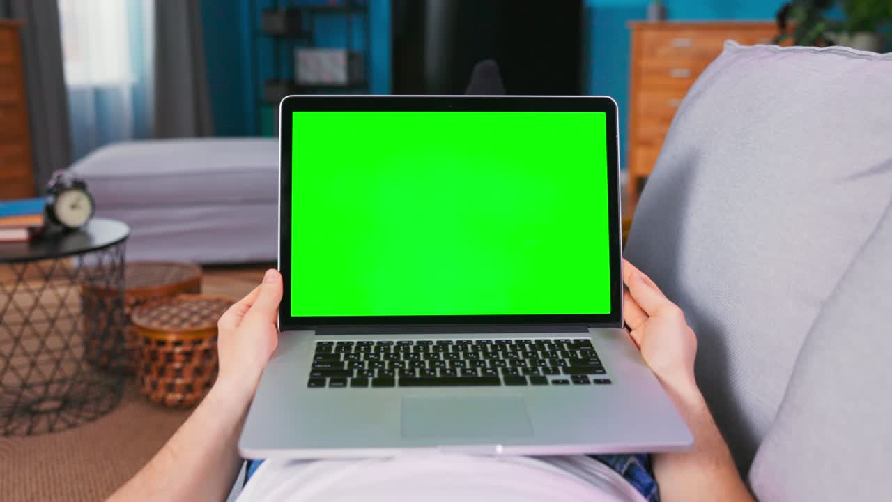 Zoom in On a Laptop with Mock-up Green Screen Display. Man is talking on video chat with friends, doctor or financial agent while is lying On a Couch in His Cozy Living Room. Point of View Camera Shot