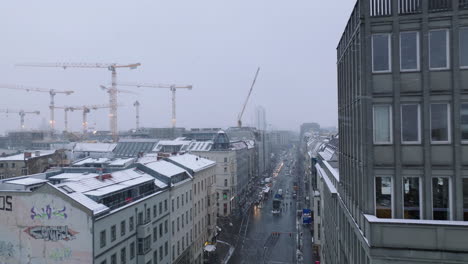 Fliegen-Sie-Im-Winter-über-Die-Straßen-In-Der-Städtischen-Nachbarschaft.-Gruppe-Von-Turmdrehkranen-Auf-Der-Baustelle.-Fallender-Schnee,-Der-Mehrstöckige-Gebäudedächer-Bedeckt.-Berlin,-Deutschland