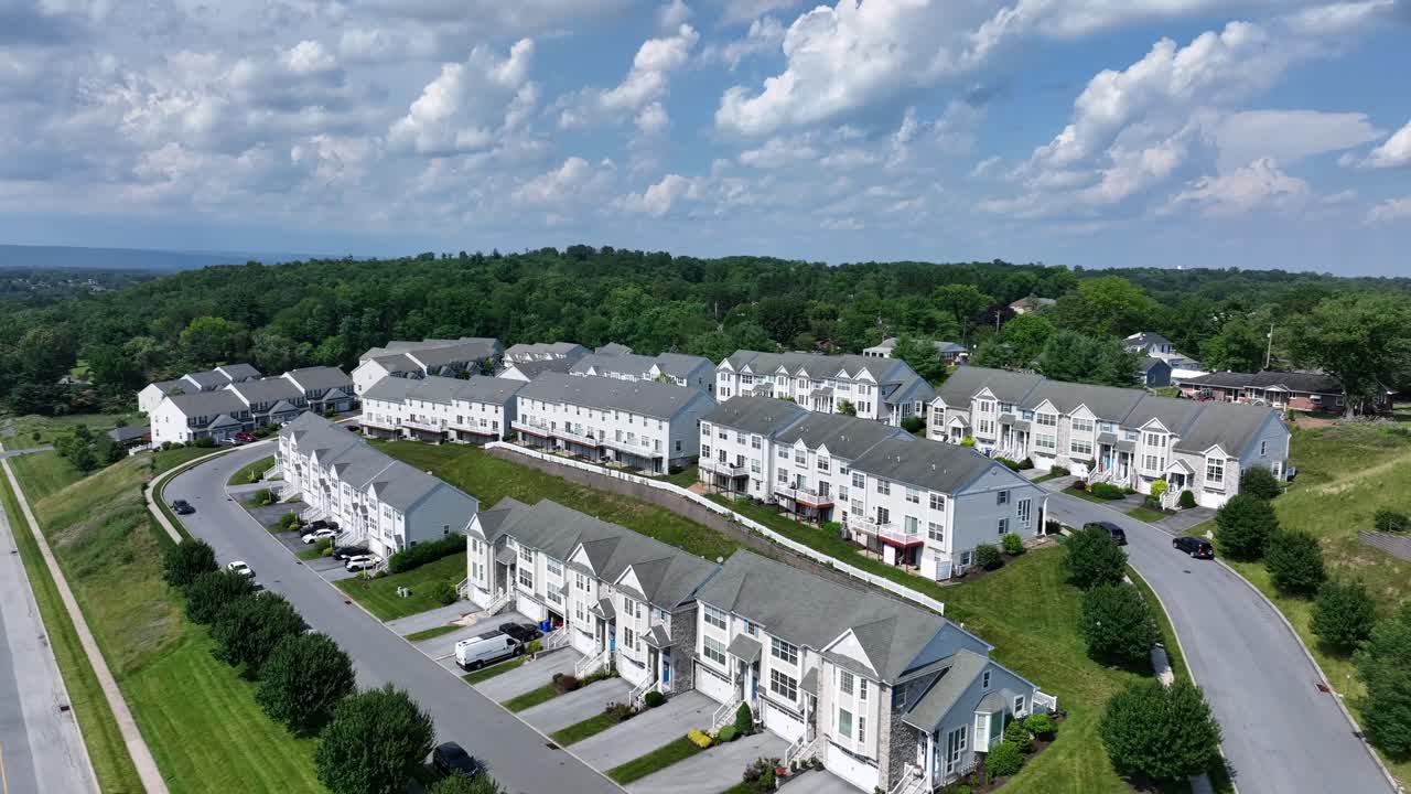 Modern suburb housing area with townhouses and residential apartments during sunny day. Aerial approaching shot. Quiet suburban neighborhood in summer. White facade and grey roof