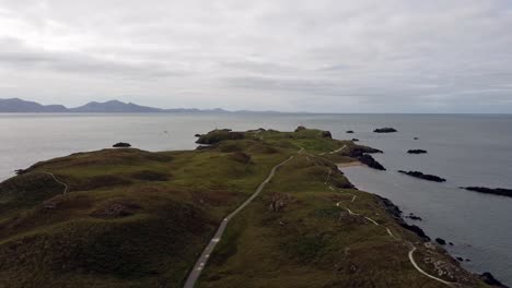 Vista-Aérea-De-La-Isla-De-Ynys-Llanddwyn,-Sendero-Costero-De-Anglesey-Con-Montañas-De-Snowdonia-A-Través-Del-Mar-De-Irlanda,-Tire-Hacia-Atrás