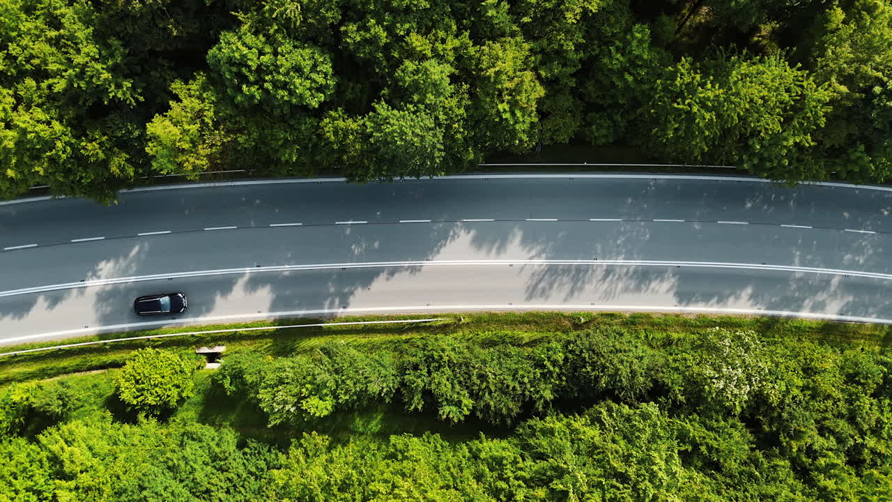 Scenic road through greenery. A vehicle navigates a winding road surrounded by dense trees and vibrant foliage in a European landscape
