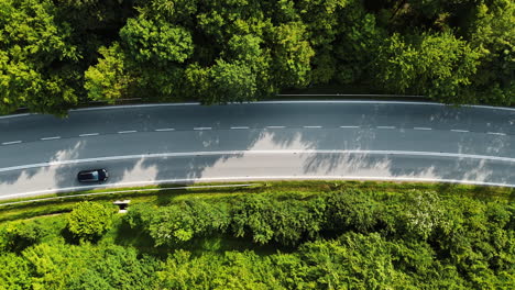 scenic road through greenery. a vehicle navigates a winding road surrounded by dense trees and vibrant foliage in a european landscape