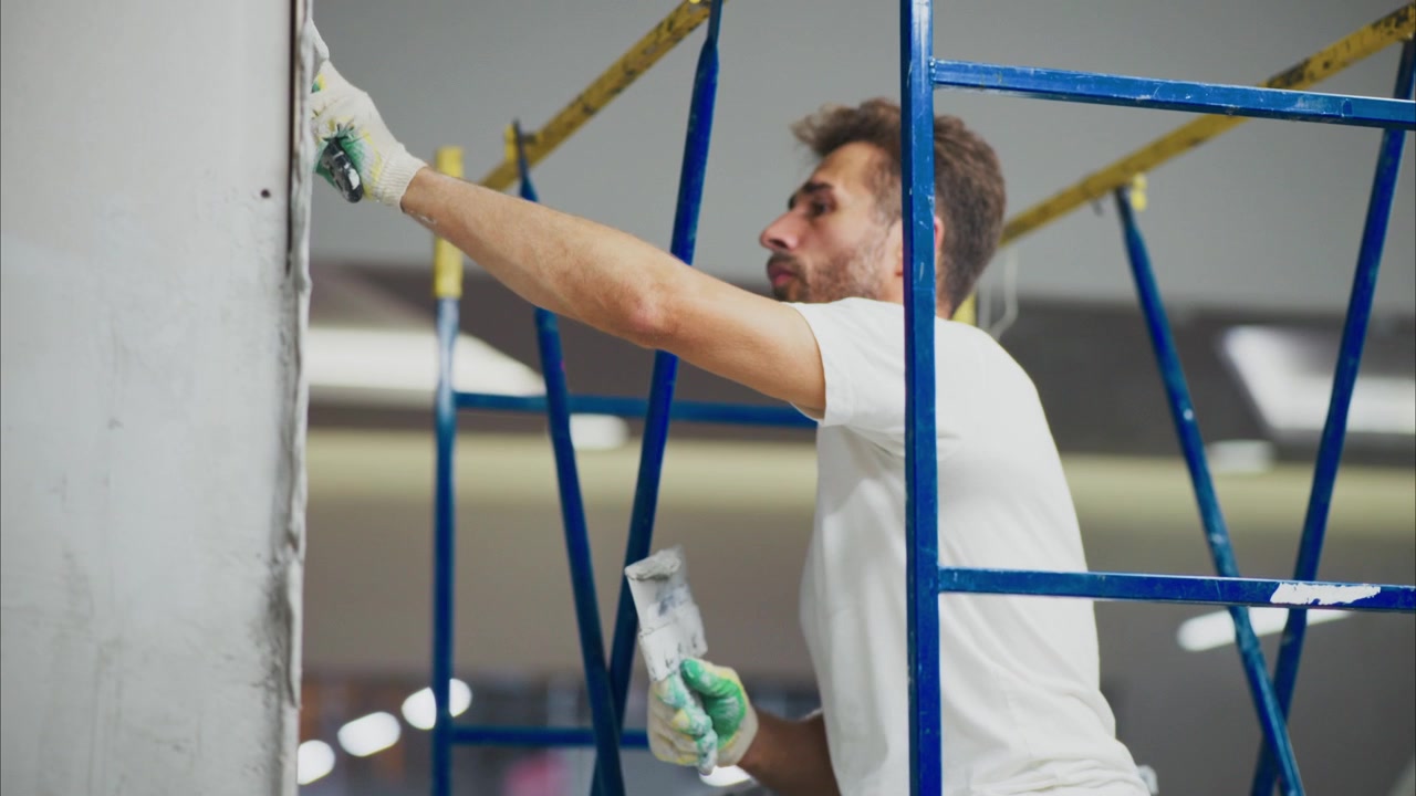 Construction Worker Applying Plaster to Wall on Scaffolding
