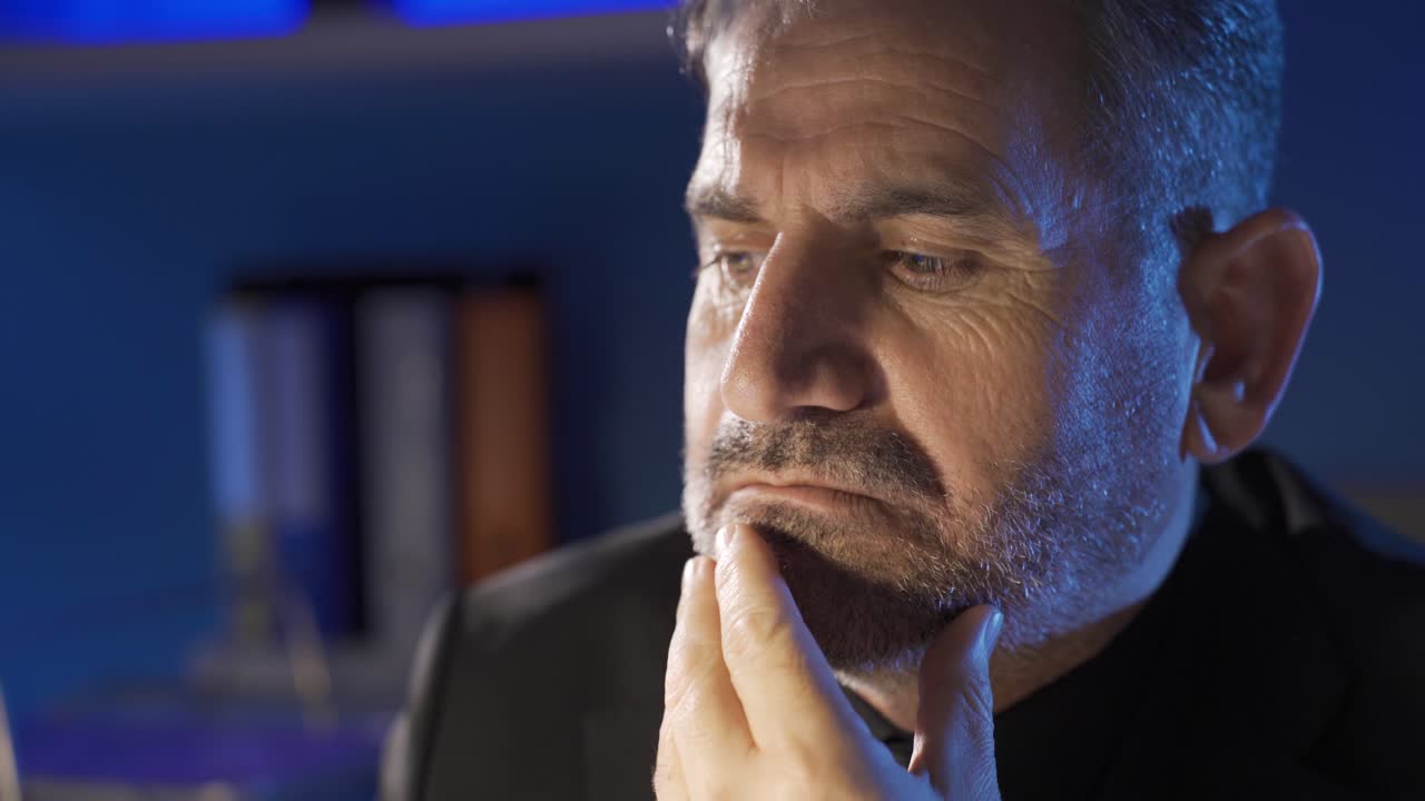 hombre de negocios maduro trabajando hasta tarde en la noche en su oficina y pensando, perdido en sus pensamientos.