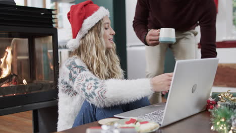 Diverse-couple-wearing-santa-hats-using-laptop-for-christmas-video-call,-in-slow-motion