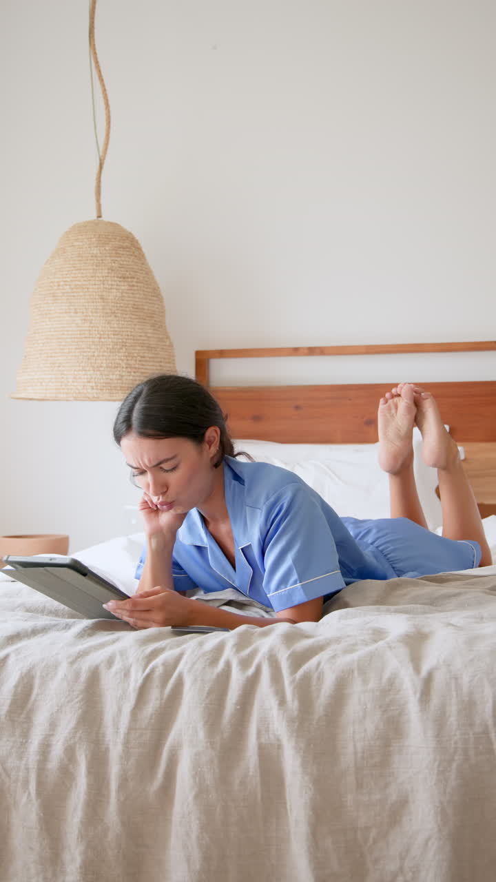 Vertical video: Relaxing at home, woman in pajamas reading book on bed, enjoying leisure time