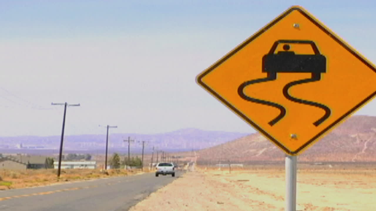 автомобили проезжают мимо скользкого от влаги дорожного знака по одинокому пустынному шоссе