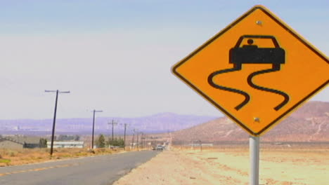 Los-Coches-Pasan-Por-Una-Señal-De-Carretera-Resbaladiza-Cuando-Está-Mojada-A-Lo-Largo-De-Una-Carretera-Del-Desierto-Solitario