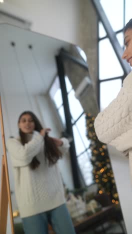 woman looking at herself in mirror, wearing a sweater, during christmas season.