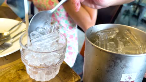 a person serves ice water from a metal bucket into a glass at a restaurant table