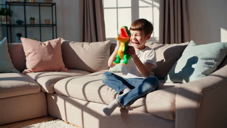 a happy young boy playing with a dinosaur toy on a couch in a sunlit living room