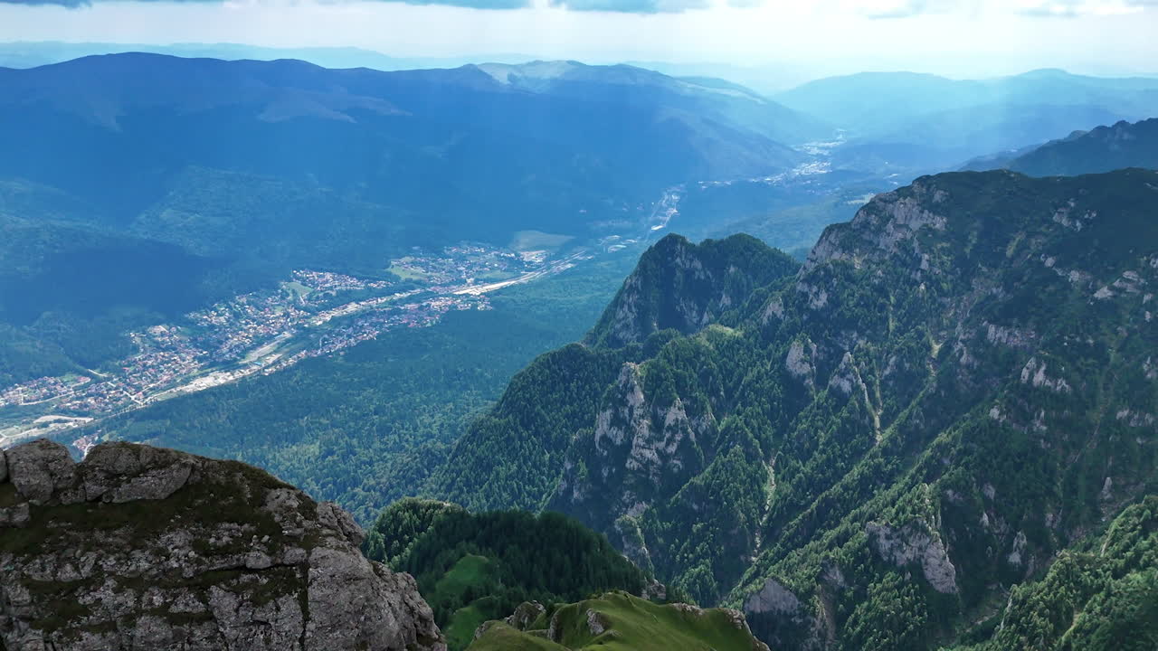 Caraiman Mountain peaks with Busteni town below. Rocky cliffs of Caraiman Mountain overlook the valley and town of Buteni in Romania