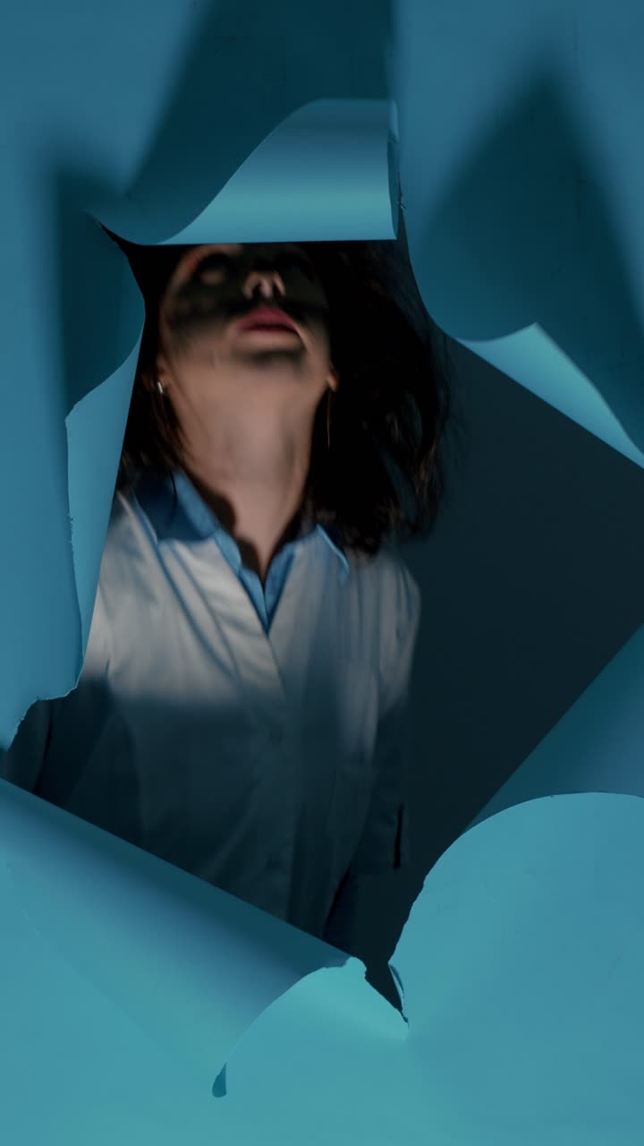 Woman with smudged makeup peering through ripped blue paper