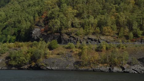 pan-left-flying-over-a-lake-in-front-of-a-autmnal-slope-with-a-car-driving-by