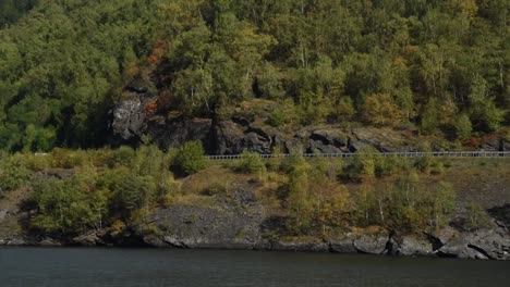 pan left flying over a lake in front of a autmnal slope with a car driving by