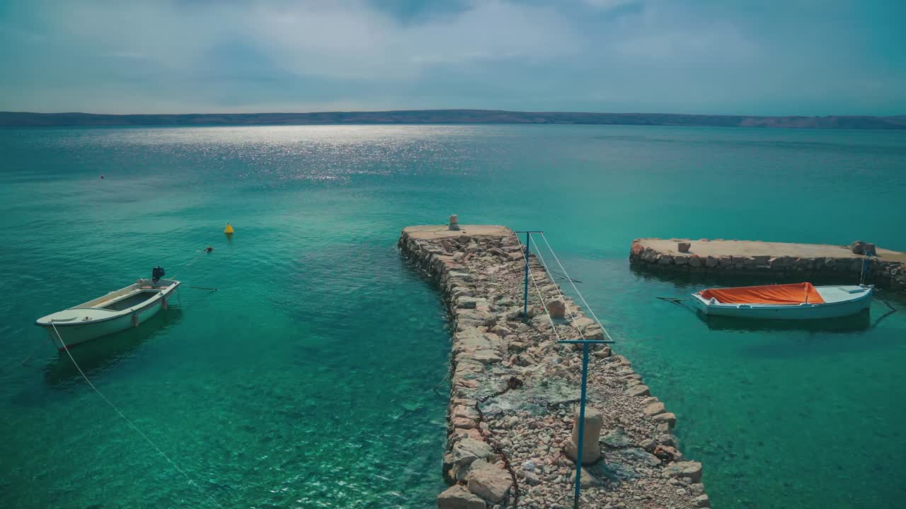 mirando un viejo puerto con dos barcos de pesca en una pintoresca playa de agua tranquila natural romántica con pequeñas olas en la costa mediterránea croata con árboles y agua azul clara. vacaciones de turismo al aire libre puesta de sol cinemagraph bucle de video sin fisuras en 4k.