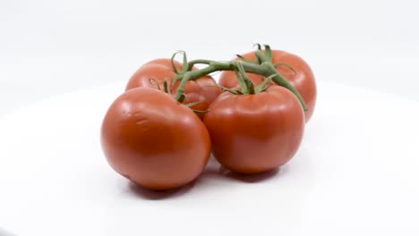 cuatro tomates maduros rojos girando sobre una plataforma blanca
