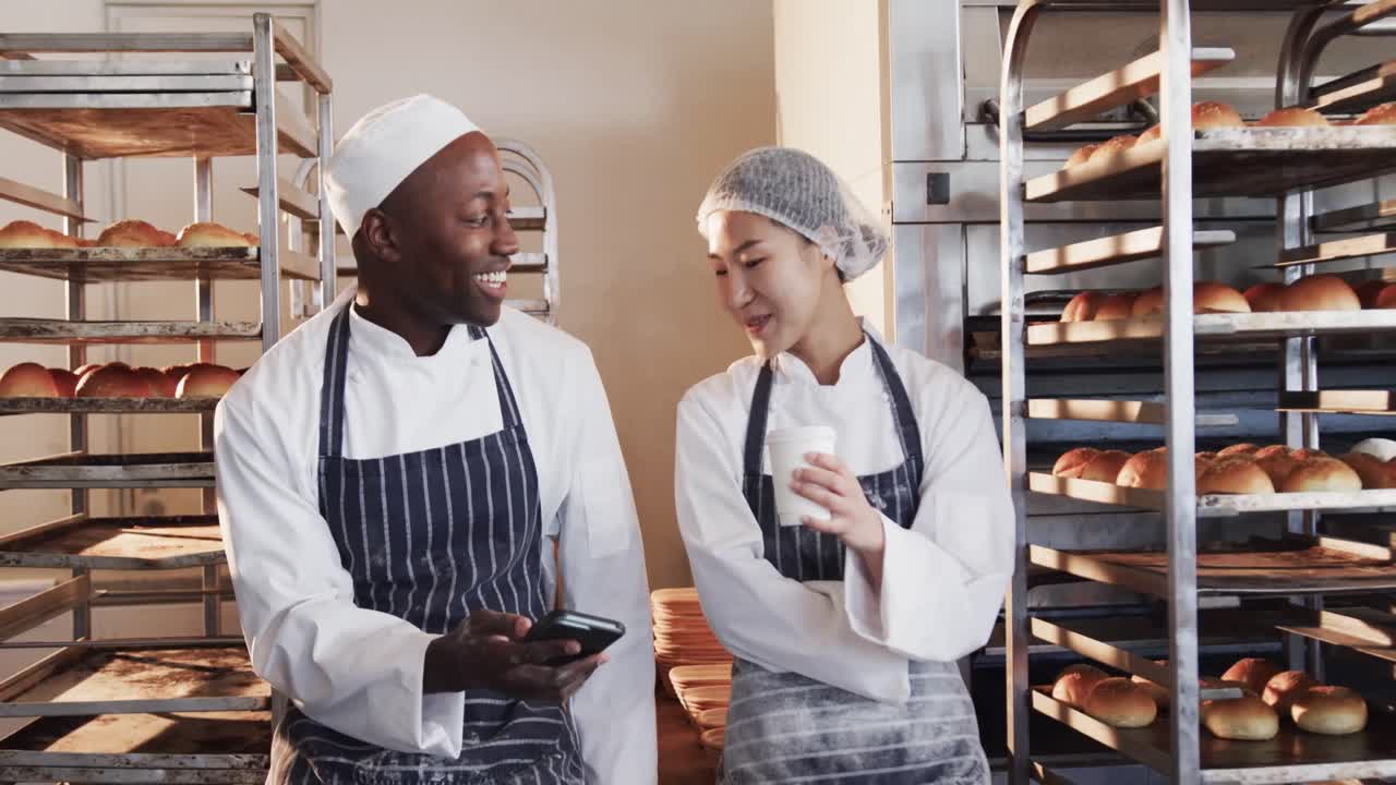 Padeiros felizes e diversos trabalhando na cozinha da padaria, usando smartphone em câmera lenta