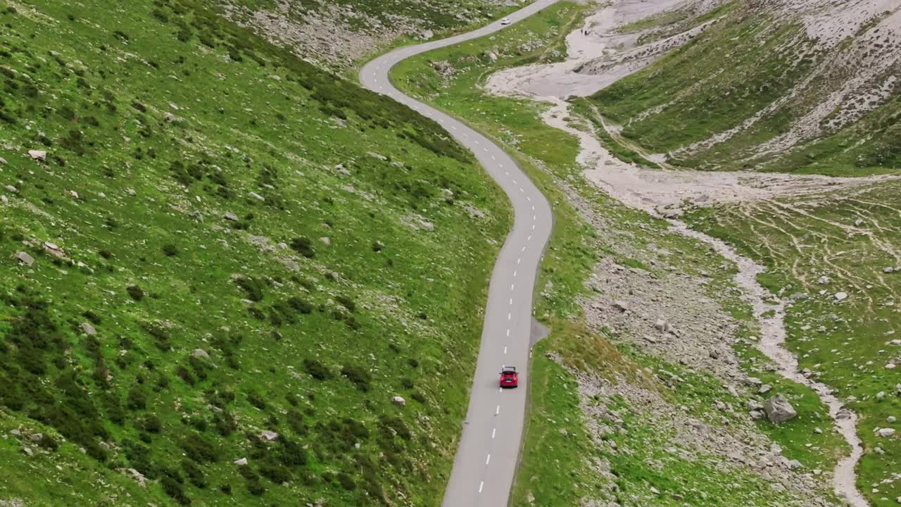 Red car with roof tent driving winding Swiss Alps mountain road aerial view