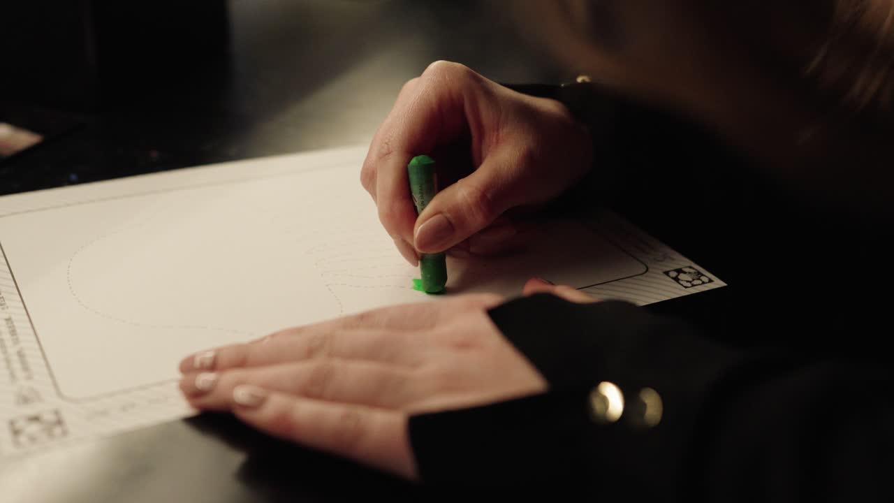 Primo piano di una persona che colora o disegna su carta con un pastello verde in un ambiente interno creativo.