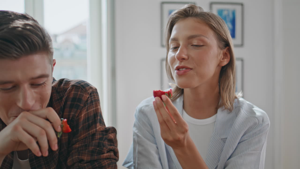 Couple enjoying strawberries together in kitchen closeup. Smiling man woman