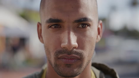 close up portrait of handsome hispanic man looking serious at camera on sunny urban city street vulnerable