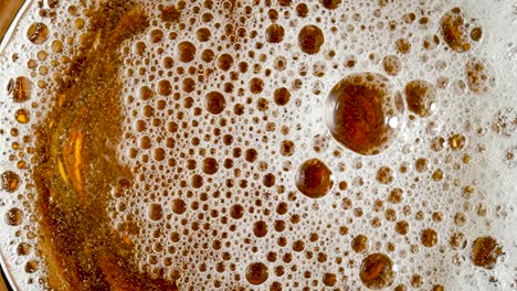 top view of golden liquid in glass with white foam and bursting bubbles top view of golden liquid in glass with white foam and bursting bubbles macro shot of an amber foamy beer cider or lagar carbonated soda or yellow oil beautiful textured beer background for advertising for pub or bar slow motion