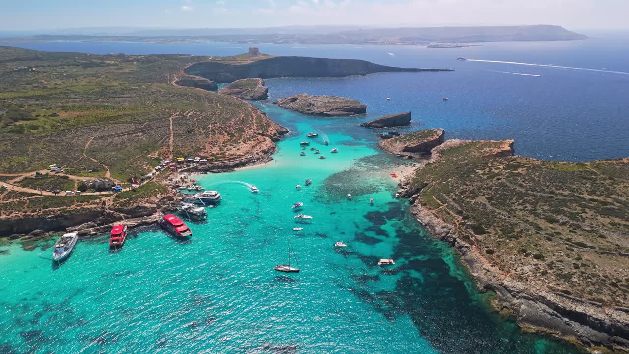 La Laguna Blu, Comino, Malta, con acque turchesi cristalline, costa rocciosa e barche ancorate è vista da una prospettiva drone in una soleggiata giornata di primavera o estate nel Mar Mediterraneo