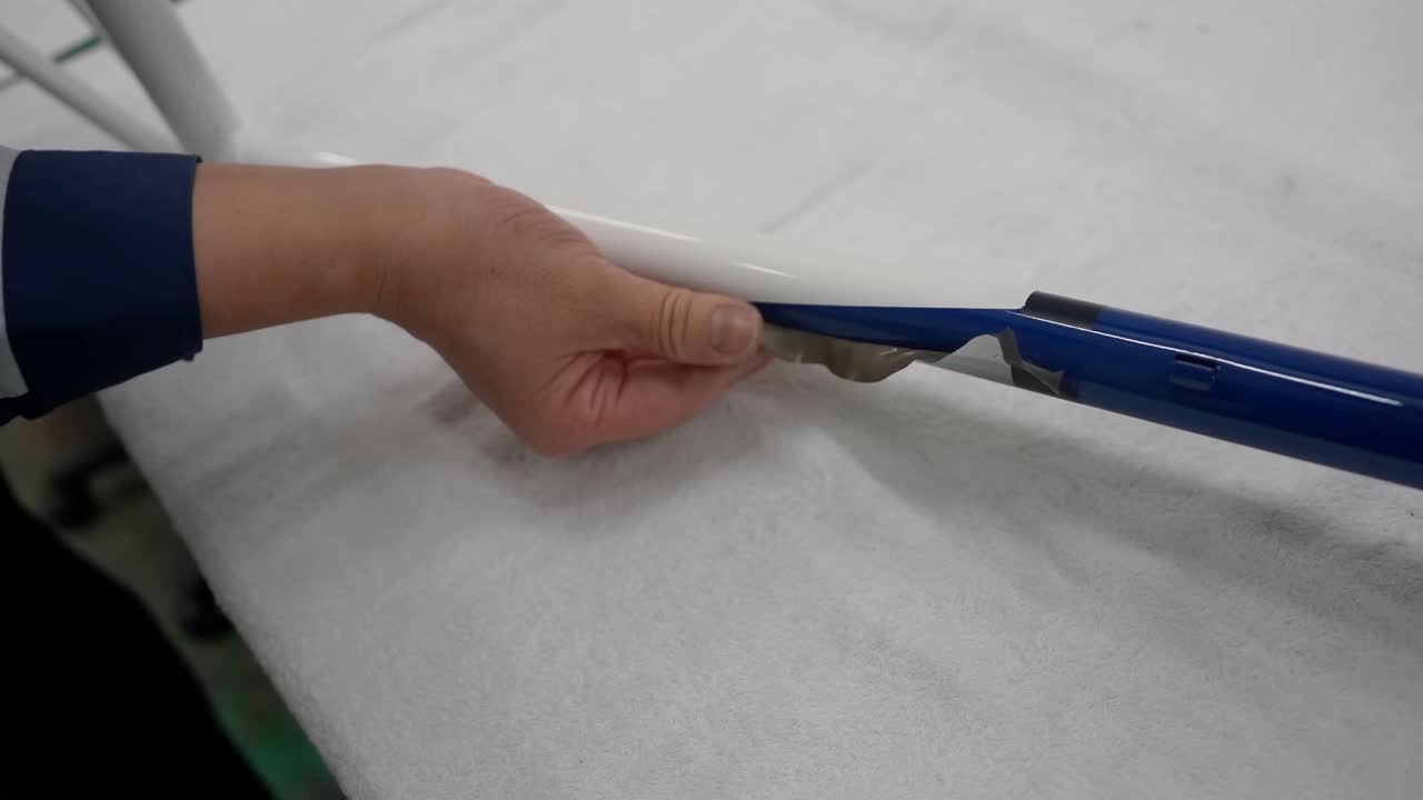 Close up of a worker's hand carefully peeling masking tape from a custom-painted blue and white bicycle frame