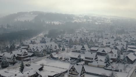 Idílico-Panorama-Aéreo-Invernal-De-Casas-De-Pueblo-De-Montaña-En-La-Nieve-Y-La-Luz-Del-Sol-Brumosa