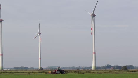 Ein-Traktor-Pflügt-Ein-Feld-Mit-Windkraftanlagen-Im-Hintergrund