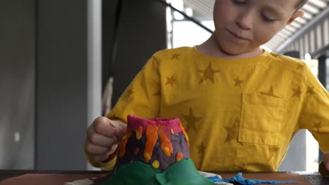 serious child creating volcano sculpture with plasticine