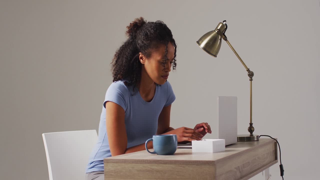 video de una mujer biracial trabajando en una computadora portátil con dolor de espalda