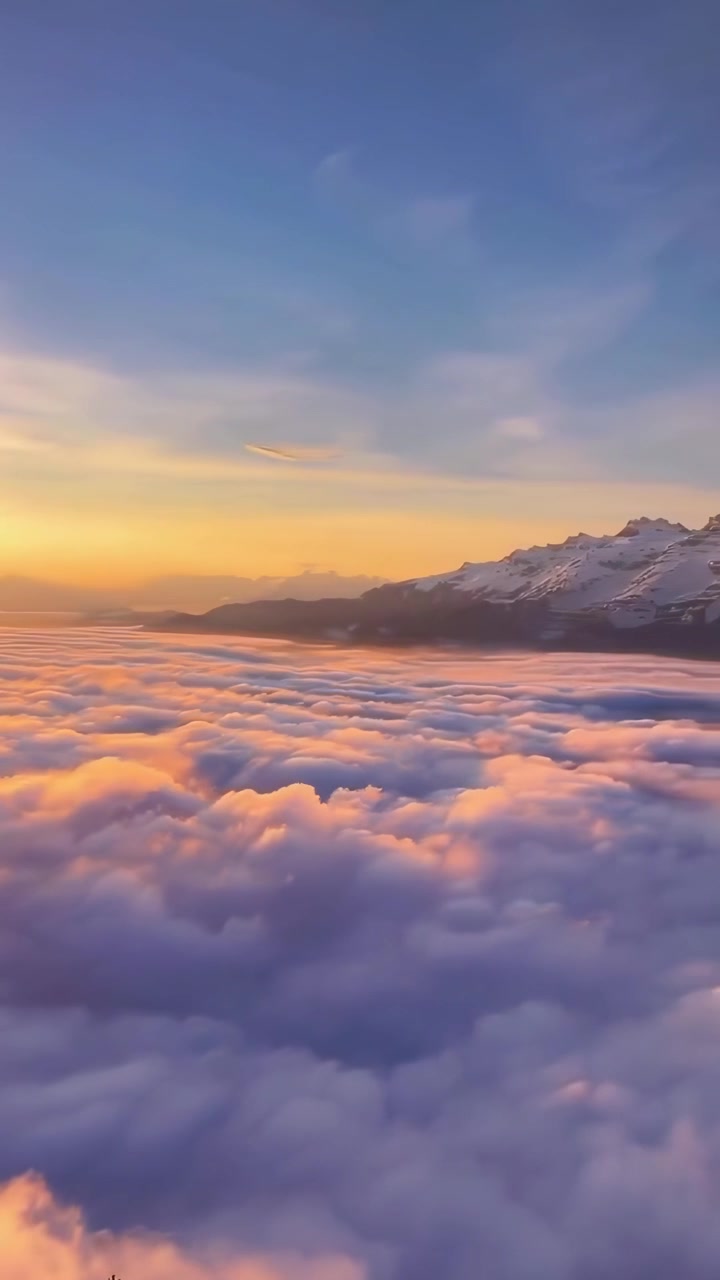 Veduta aerea di montagne innevate sopra un mare di nuvole al tramonto