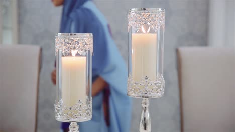 muslim woman places lighted candles in elegant glass candle holders on the table - medium shot