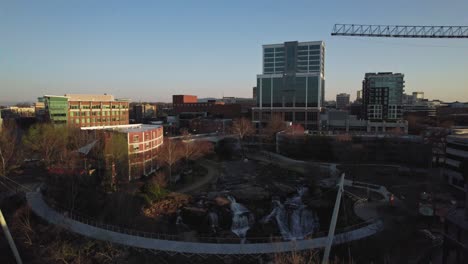 Drone-flying-away-and-above-waterfall-and-city-skyline-during-sunrise