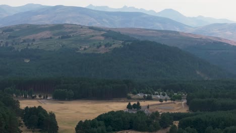 drone flying behind a mountainous landscape of the sierra de gredos, in the distance you can see the highest peaks, there are wild pine forests and a meadow with dry grass because it is summer