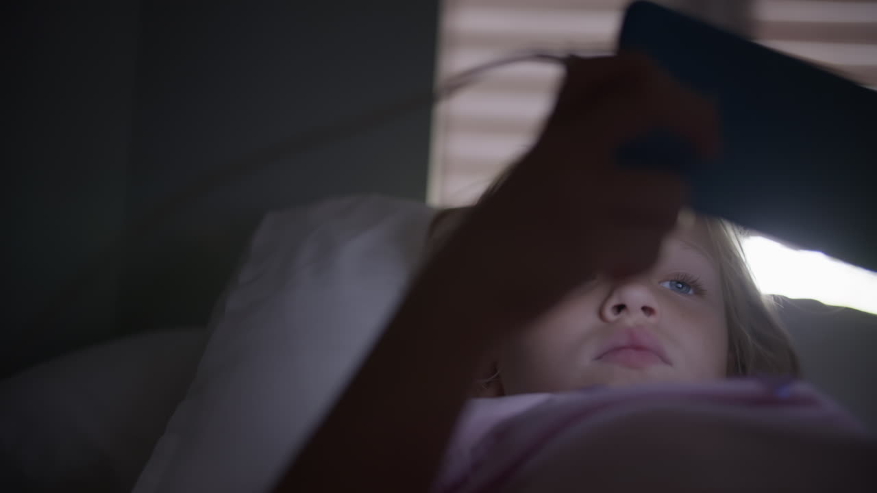 어린 소녀가 침대에서 전화로 놀고 있다