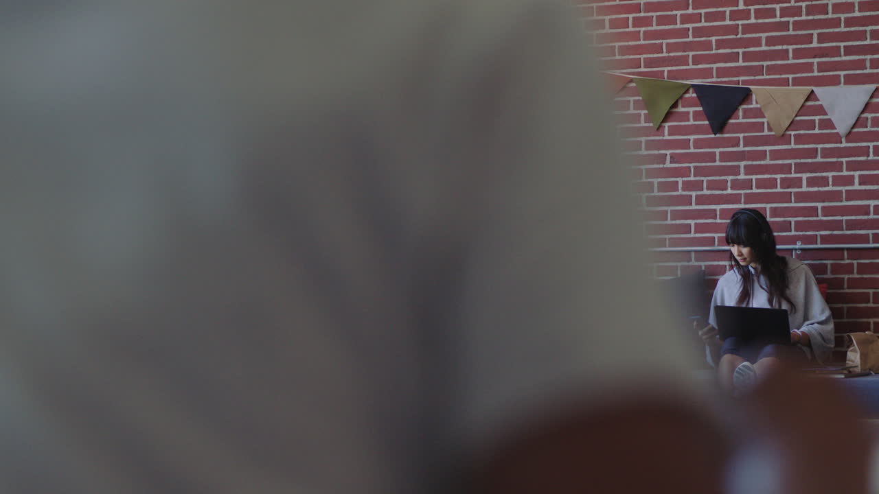 joven mujer de negocios asiática usando computadora portátil estudiante trabajando en un proyecto estudiando revisando mensajes en el teléfono inteligente disfrutando de un lugar de trabajo de oficina relajado escuchando música