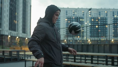 athlete skillfully juggling ball with knee in urban outdoor sport arena, displaying concentration and athleticism, background includes modern buildings, benches, and exercise equipment