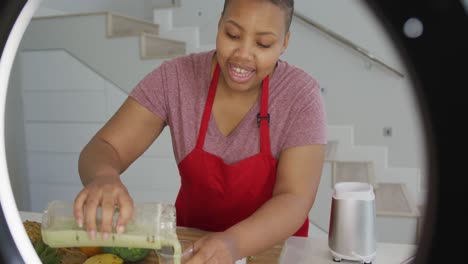 happy african american plus size woman wearing apron, making cooking vlog with camera in kitchen