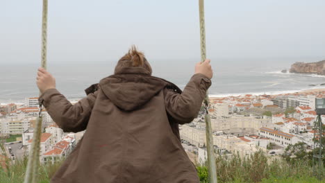 Chico-En-El-Columpio-Contra-El-Océano-Y-La-Costa-En-Nazaré,-Portugal