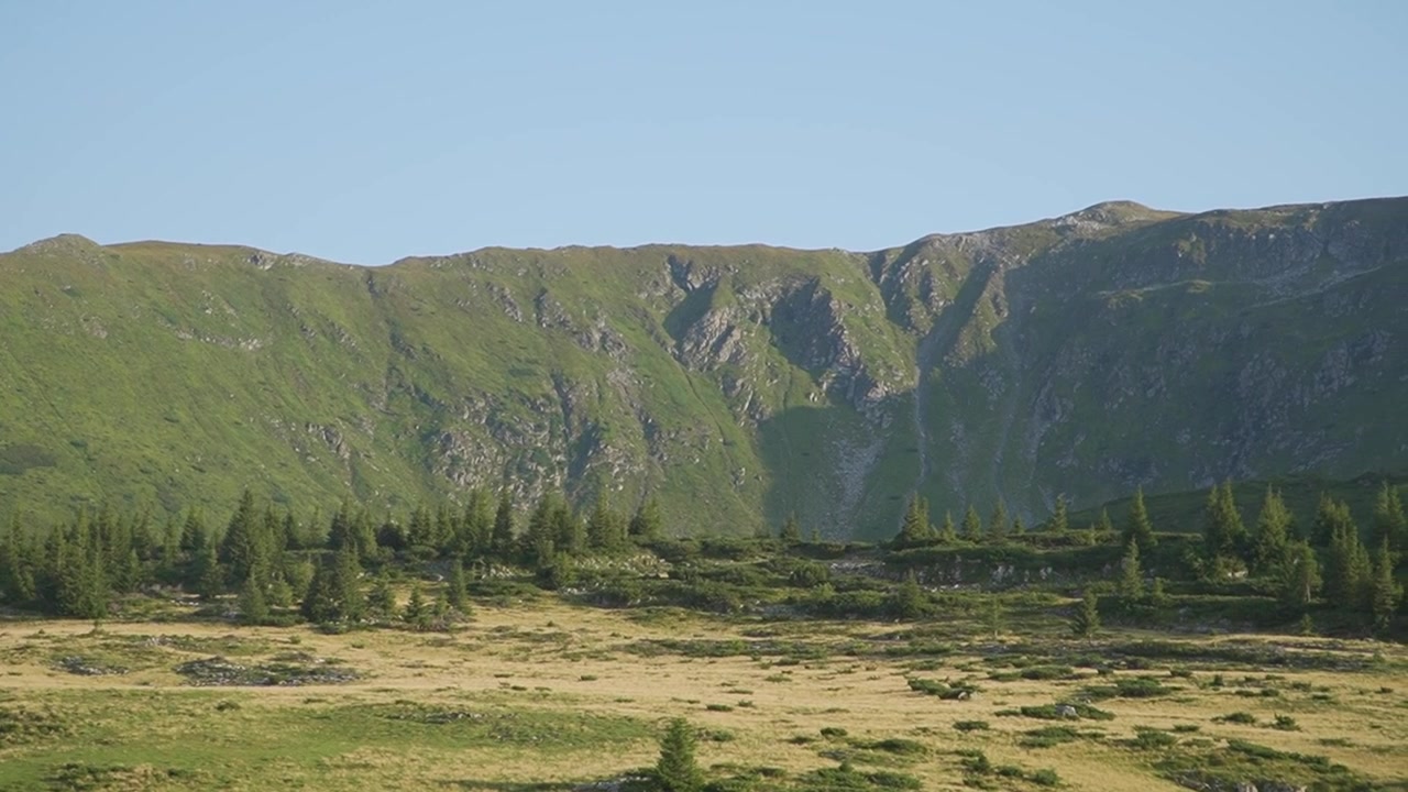Stort bjergområde med grønne alpeskråninger og en vild eng. Naturskønt vildmarkslandskab perfekt til rejse- og udforskningsindhold.